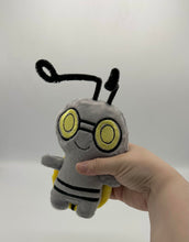 Load image into Gallery viewer, Little grey monster plush with yellow eyes and black stripes on his body. He has long thin black antenna and a yellow coin on his back!