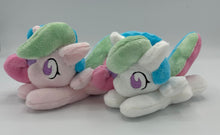 Load image into Gallery viewer, Pink horse plush laying on belly with sun on flank and blue/pink/purple/green hair. Eye is purple. She is with her white counterpart. 
