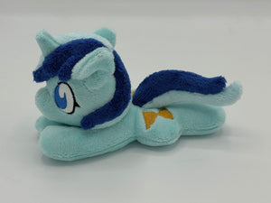 Blue horse plush laying on belly with gold hourglass on flank and two tone blue hair. Eye is blue.