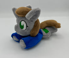 Load image into Gallery viewer, Grey horse plush laying on belly with green square on flank and two brown hair. Eye is green. Wears a blue shirt.
