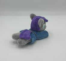 Load image into Gallery viewer, Grey horse plush laying on belly with purple hair. Eye is blue. Wears a blue dress with a grey belt
