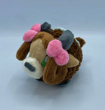 Load image into Gallery viewer, A brown yak plush. She has a furry dark brown coat and four grey hooves. She has a dark brown fluffy tail. She wears a green blanket on her back. She has a lighter brown face with pointed brown ears. She has grey horns. She has darker hair that is worn in two brown loops. She has two pink bows on her hair. Her muzzle is cream with a grey nose shaped like an oval. Her eyes are green. 
