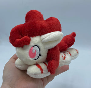 Cream colored horse plush with red stripes laying on belly with red candy canes shaped like a heart on flank and red hair. Eye is pink.