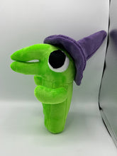 Load image into Gallery viewer, A green monster plush that has a huge mouth and nose. He has a big eye and wears a purple witch hat. 
