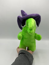 Load image into Gallery viewer, A green monster plush that has a huge mouth and nose. He has a big eye and wears a purple witch hat. 
