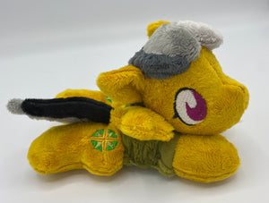 Gold colored horse plush laying on belly with green and gold compass on flank and her hair is grey shades. Eye is maroon. Wears a green shirt and safari hat
