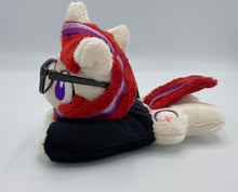Load image into Gallery viewer, Cream colored horse plush laying on belly with purple moon and pink stars on flank and red hair with purple stripes. Eye is purple. Wears a black shirt and glasses
