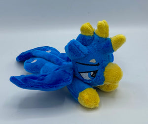 Blue gryphon plush laying on belly. Has a cream belly. Tail is a long lion tail tipped in dark blue. Has dark blue wings. Back feet are paws and front feet are yellow like bird feet. Has a yellow beak and a blue eye. Has feathers on had that are blue and yellow. Ears are blue and look like feathers. 