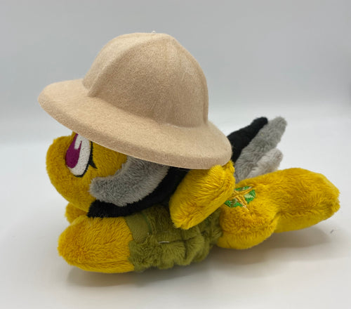 Gold colored horse plush laying on belly with green and gold compass on flank and her hair is grey shades. Eye is maroon. Wears a green shirt and safari hat