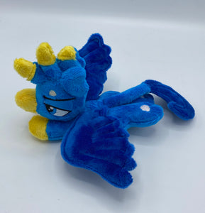 Blue gryphon plush laying on belly. Has a cream belly. Tail is a long lion tail tipped in dark blue. Has dark blue wings. Back feet are paws and front feet are yellow like bird feet. Has a yellow beak and a blue eye. Has feathers on had that are blue and yellow. Ears are blue and look like feathers. 