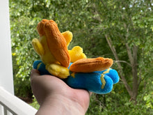 Load image into Gallery viewer, Blue body with yellow head horse plush laying on belly with yellow zigzag on flank and feet and has orange hair. Eye is brown.
