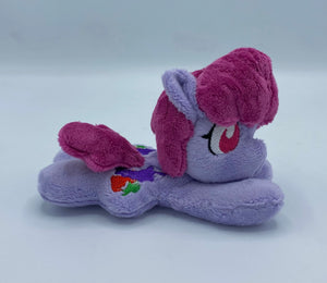 Purple horse plush laying on belly with colorful fruit on flank and maroon hair. Eye is red.
