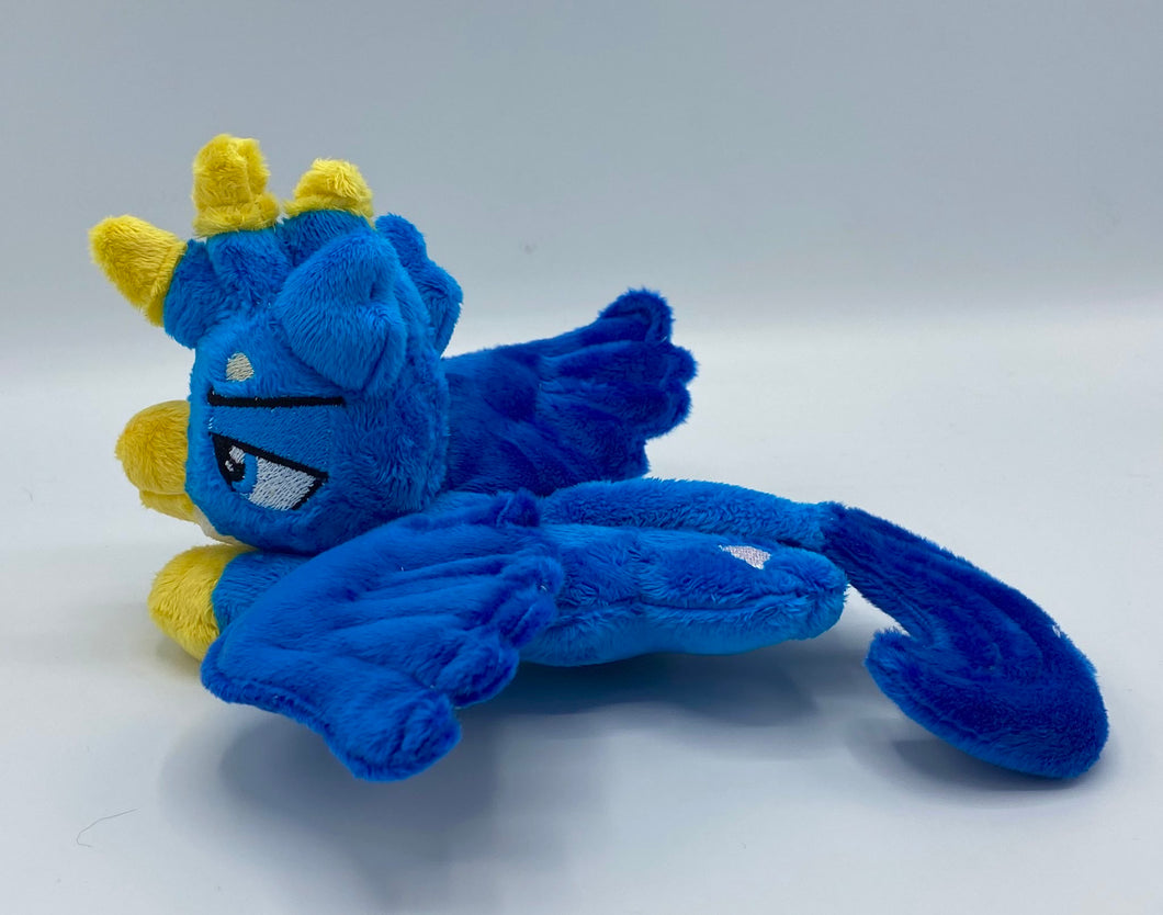 Blue gryphon plush laying on belly. Has a cream belly. Tail is a long lion tail tipped in dark blue. Has dark blue wings. Back feet are paws and front feet are yellow like bird feet. Has a yellow beak and a blue eye. Has feathers on had that are blue and yellow. Ears are blue and look like feathers. 