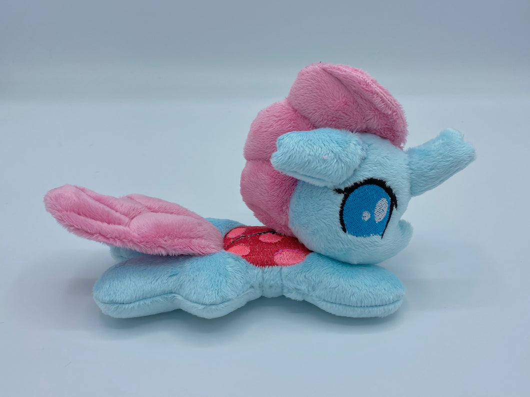 Blue changeling plush (looks just like a horse) laying on belly with pink and red ladybug design on back and pink hair. Eye is blue.