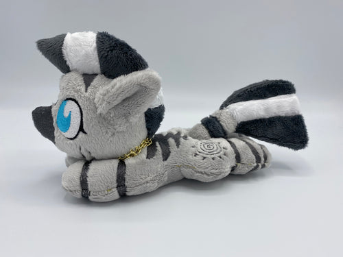 A zebra plush laying on belly. The coat is grey with black stripes. There is a grey sun design on the flank. She has a dark grey muzzle. Hair is white and grey stripes. Eye is blue. She has a gold chain around her neck. 