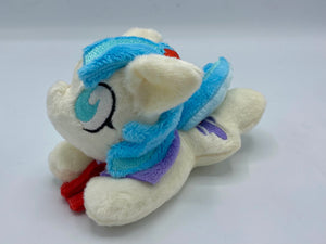 Cream horse plush laying on belly with purple hat on flank and two tone blue hair. Eye is blue. Has flower in hair. 