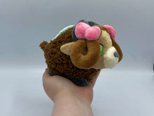 Load image into Gallery viewer, A brown yak plush. She has a furry dark brown coat and four grey hooves. She has a dark brown fluffy tail. She wears a green blanket on her back. She has a lighter brown face with pointed brown ears. She has grey horns. She has darker hair that is worn in two brown loops. She has two pink bows on her hair. Her muzzle is cream with a grey nose shaped like an oval. Her eyes are green. 

