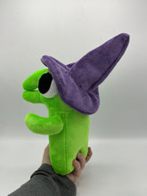 Load image into Gallery viewer, A green monster plush that has a huge mouth and nose. He has a big eye and wears a purple witch hat. 
