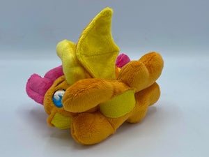 Orange dragon plush laying on belly. She is orange with a yellow belly. Her wings are orange and yellow. Her horns are yellow. She has pink hair. Her tail is orange and yellow with a pink tip. Her mouth is yellow. Her eyes are blue. She has brown eyebrows. 