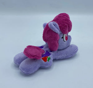 Purple horse plush laying on belly with colorful fruit on flank and maroon hair. Eye is red.