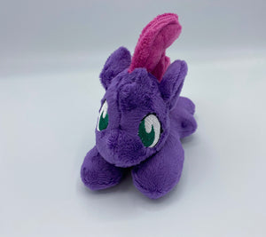 Purple colored horse plush laying on belly with maroon Mohawk hair. Eye is green. 